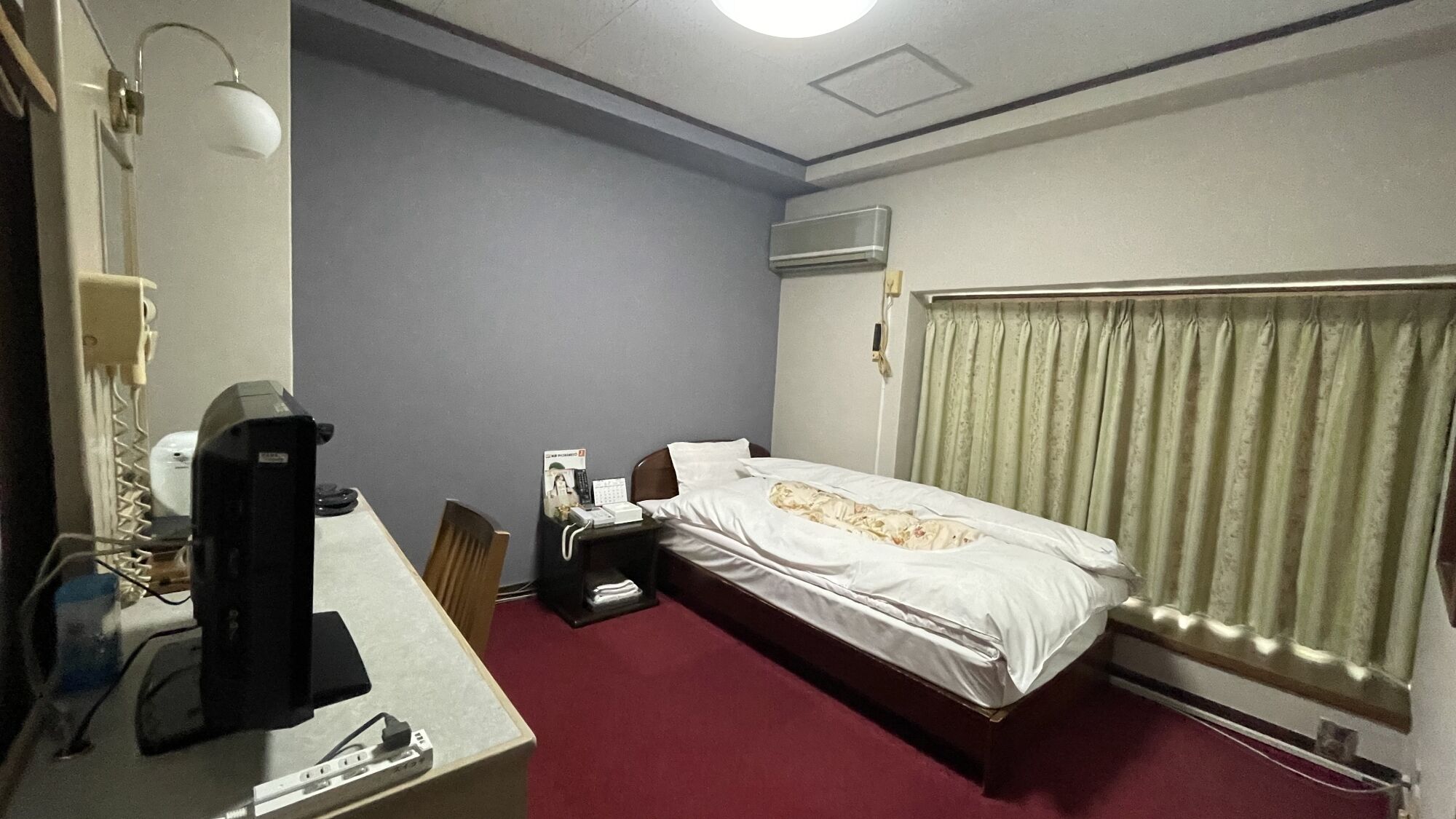 Ein Hotelzimmer mit einem Bett, einem Schreibtisch mit Computer, einem Telefon und einer Klimaanlage.