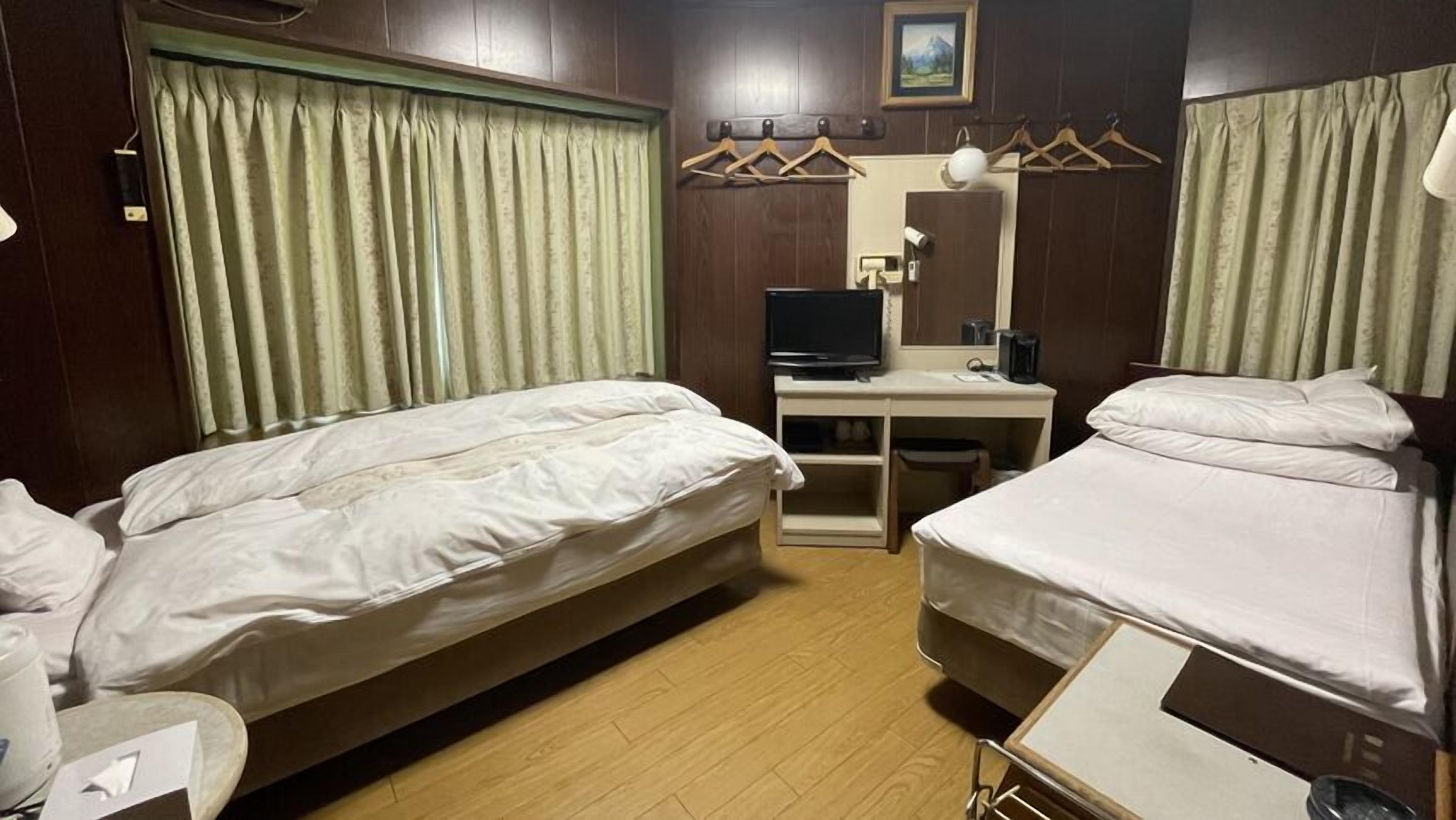 A hotel room with two beds, a desk with a computer, a mirror, and a window with curtains.