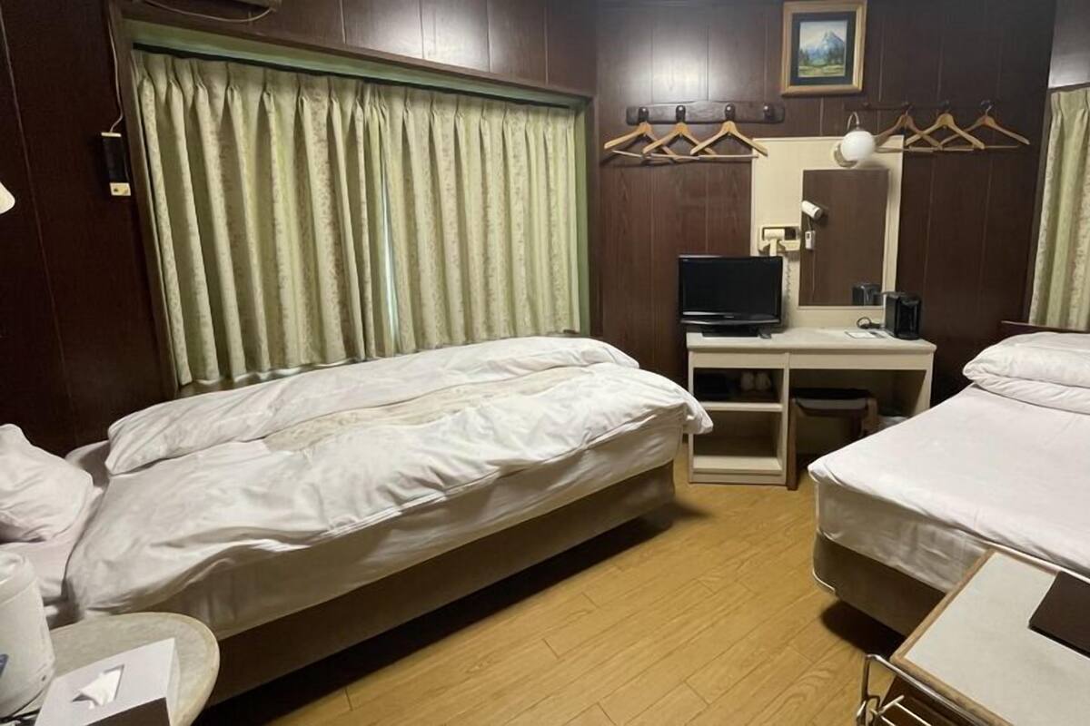 A hotel room with two beds, a desk with a computer, a mirror, and a window with curtains.