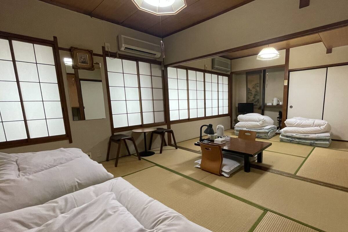 A traditional Japanese room with tatami flooring, a futon bed, a small table with a lamp, and a TV.