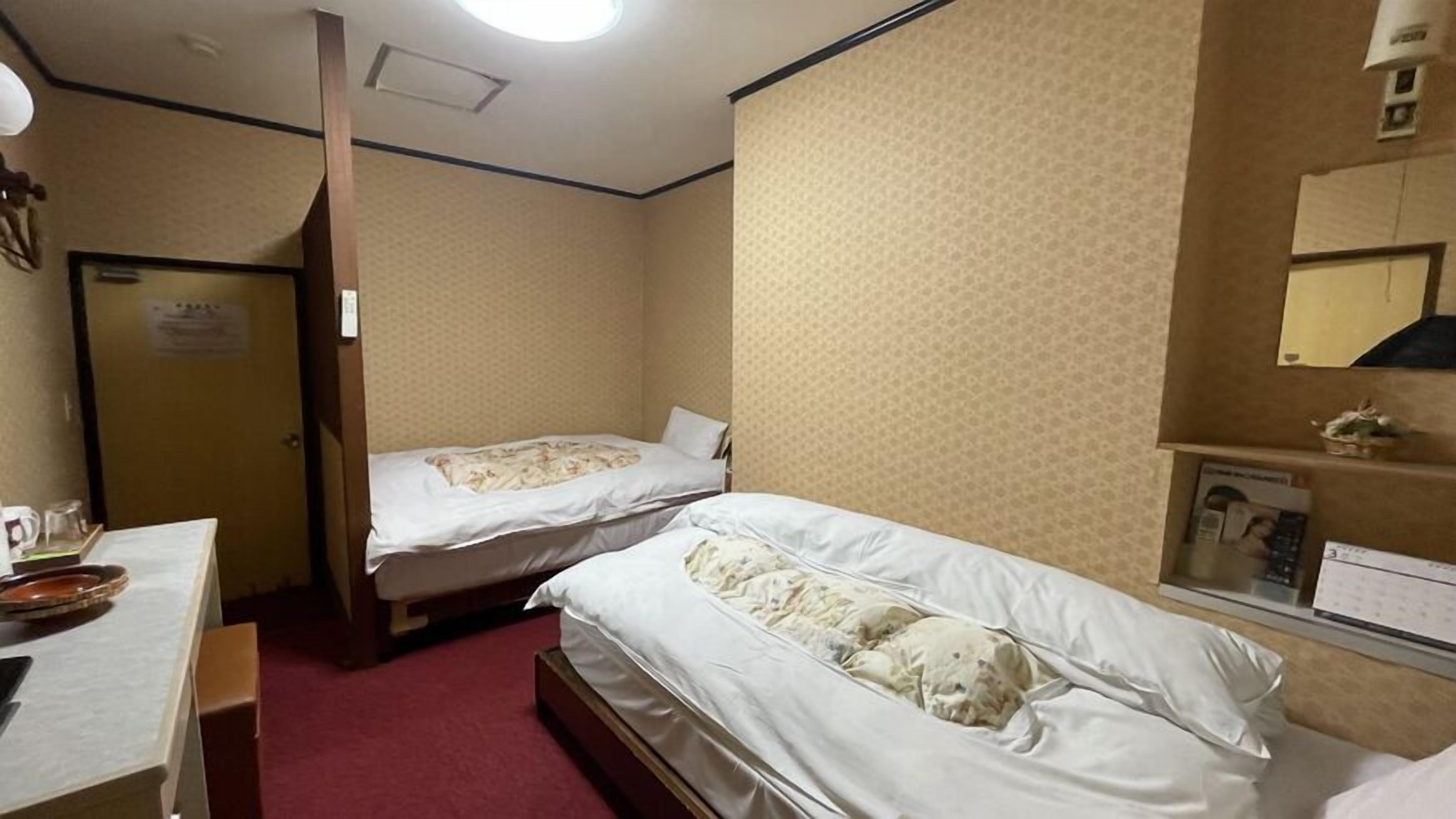 A hotel room with two beds, a desk, a mirror, and a door.