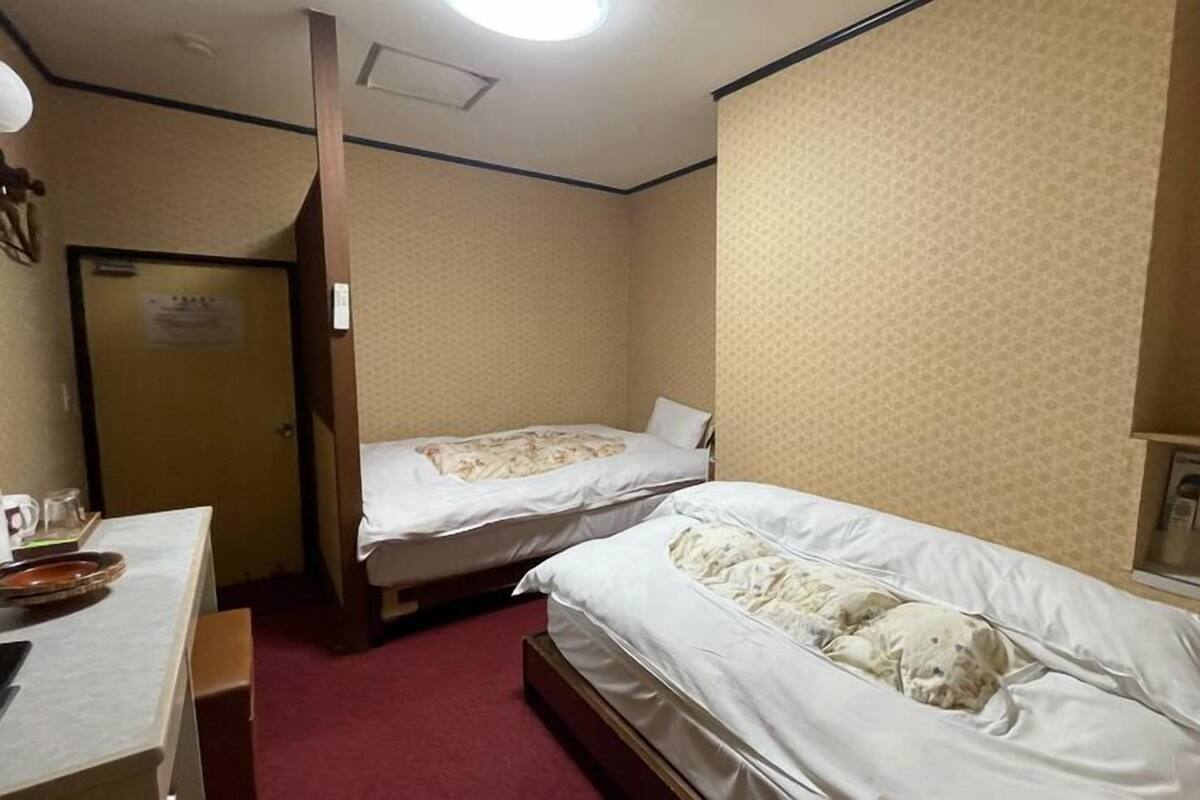 A hotel room with two beds, a desk, a mirror, and a door.