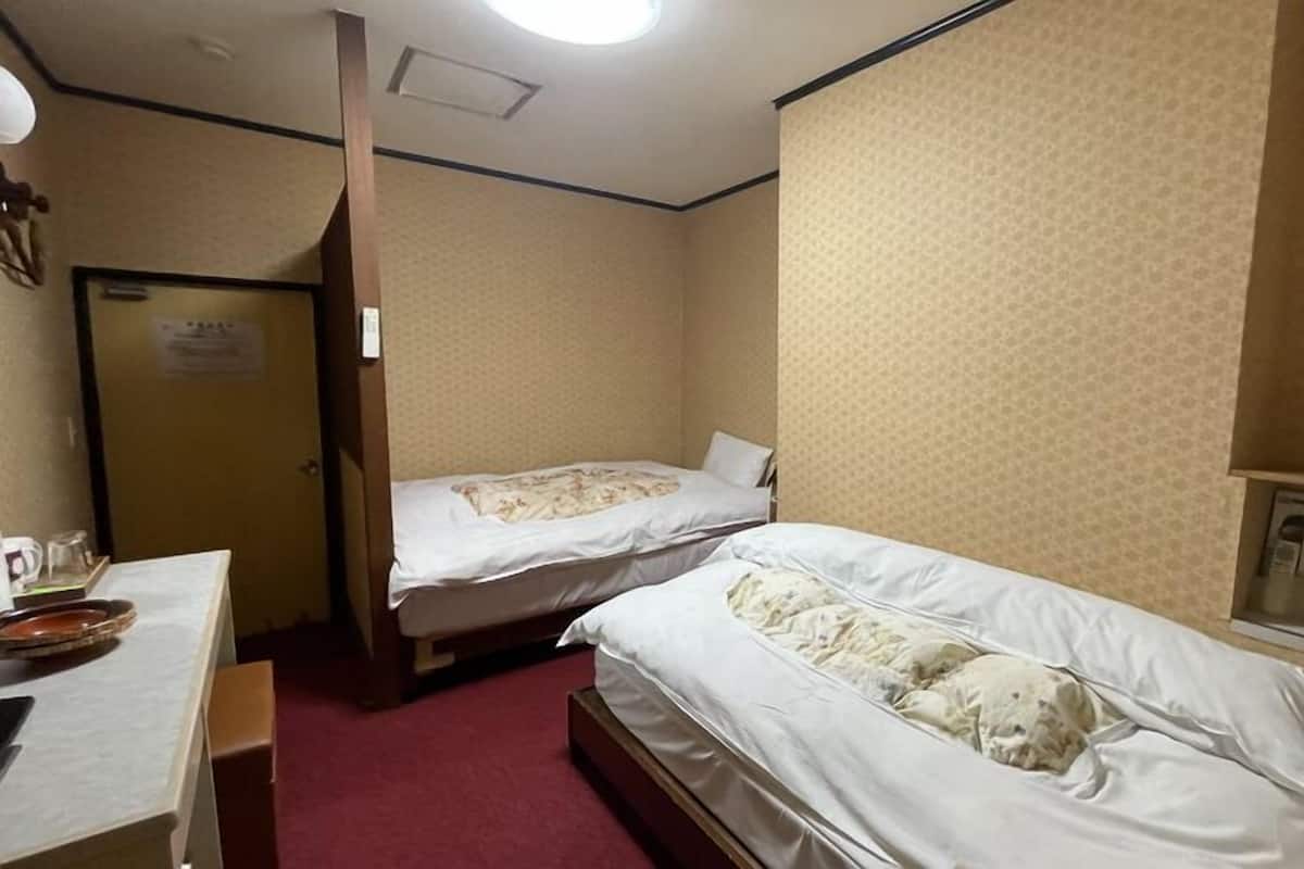 A hotel room with two beds, a desk, a mirror, and a door.