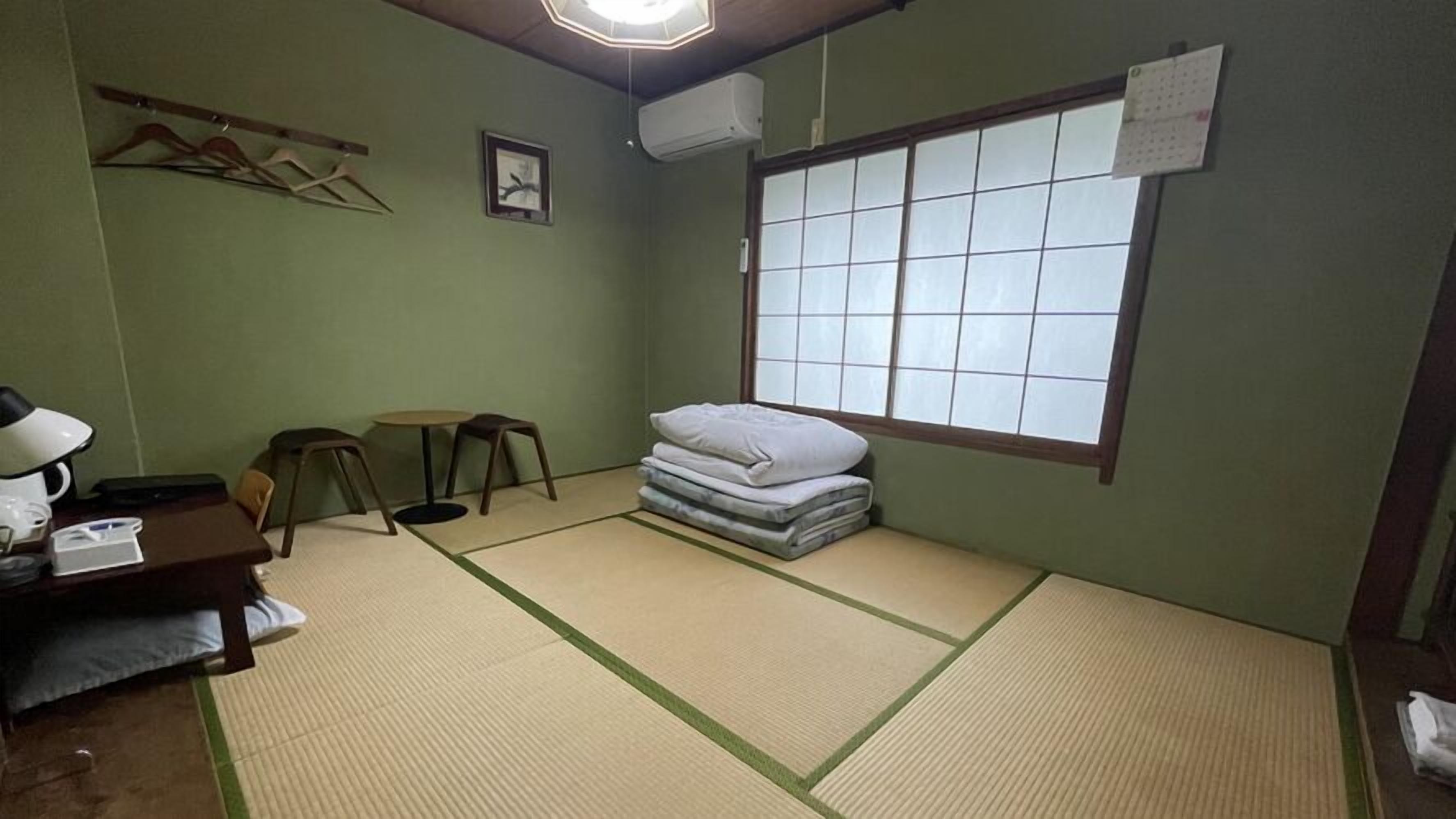 A room with tatami mats, a futon, a desk with a lamp, and a window with a view.