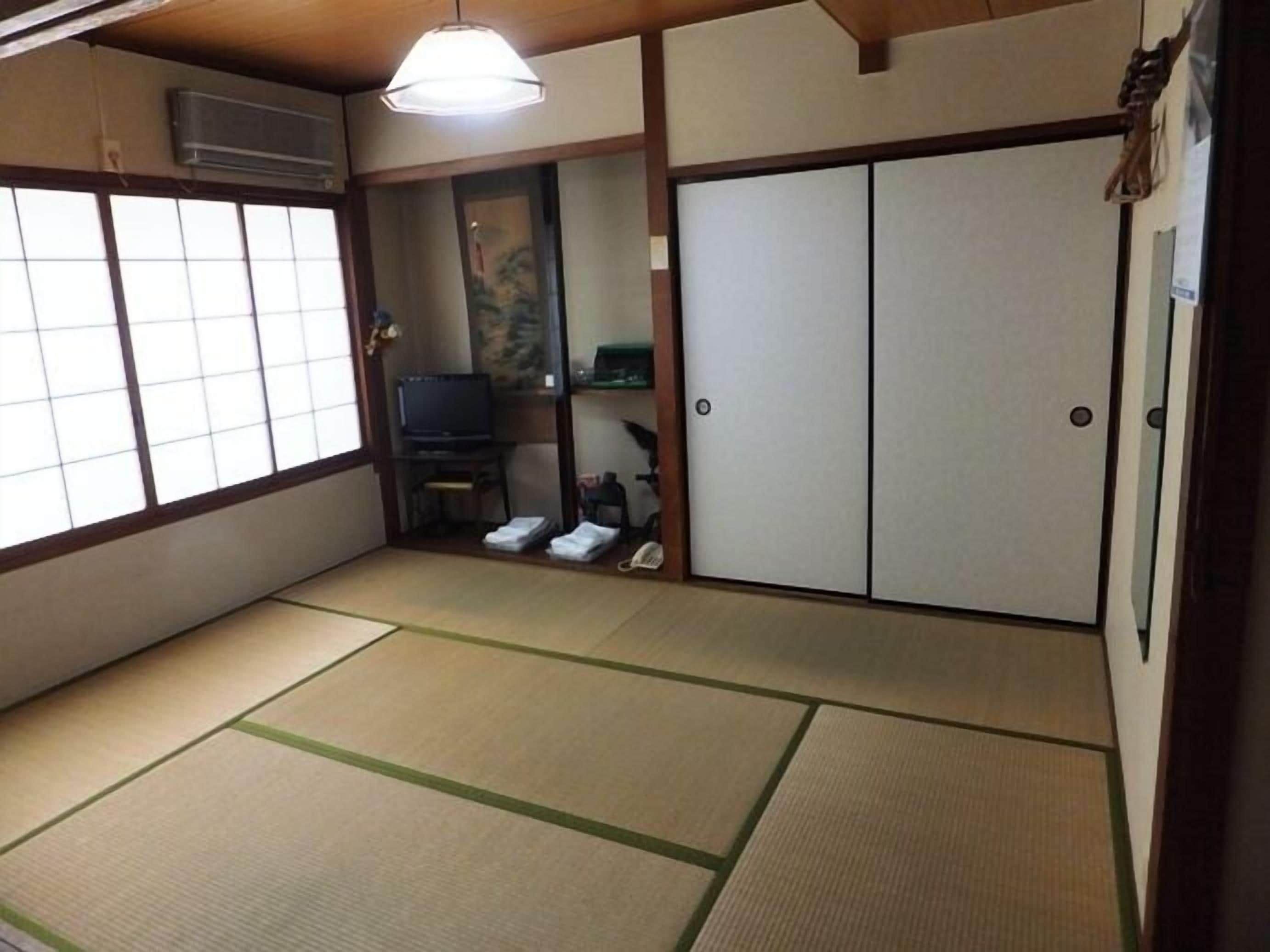 Ein traditioneller japanischer Raum mit Tatami-Böden, Schiebetüren, einem Fernseher und einem kleinen Regal.