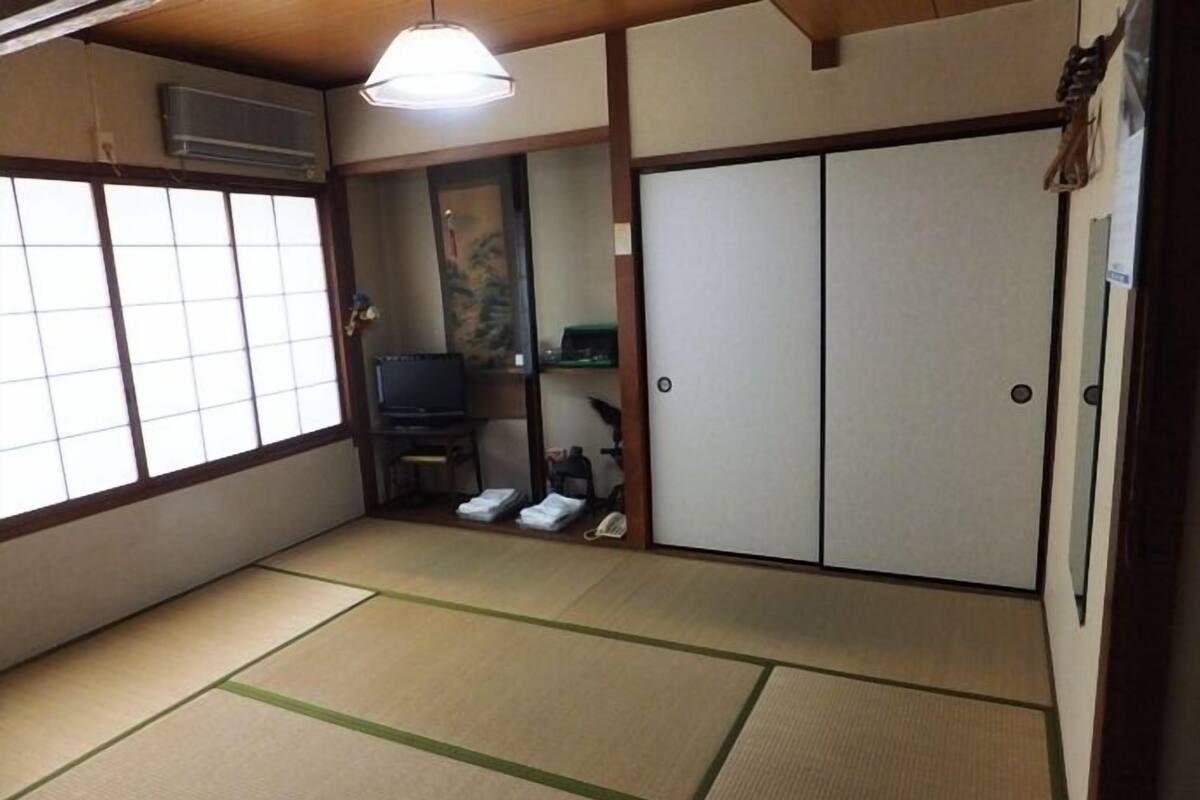 A traditional Japanese room with tatami flooring, sliding doors, a television, and a small shelf.