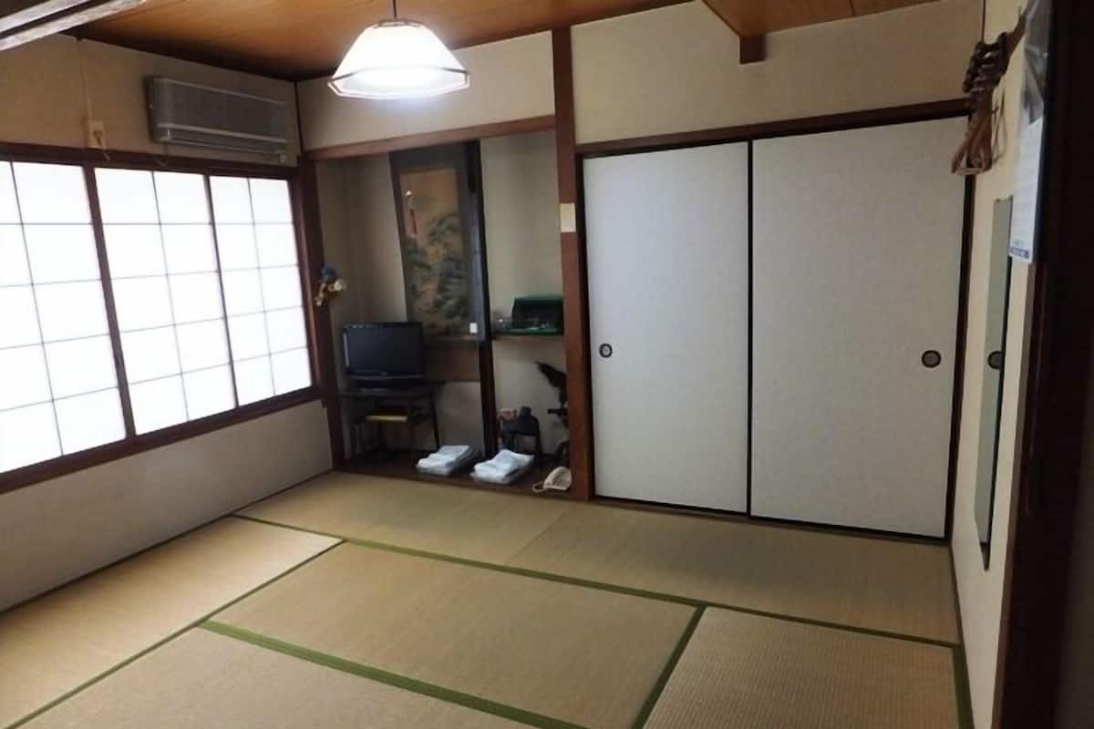 Et traditionelt japansk rum med tatamimåtter, skydedøre, et fjernsyn og en lille hylde.