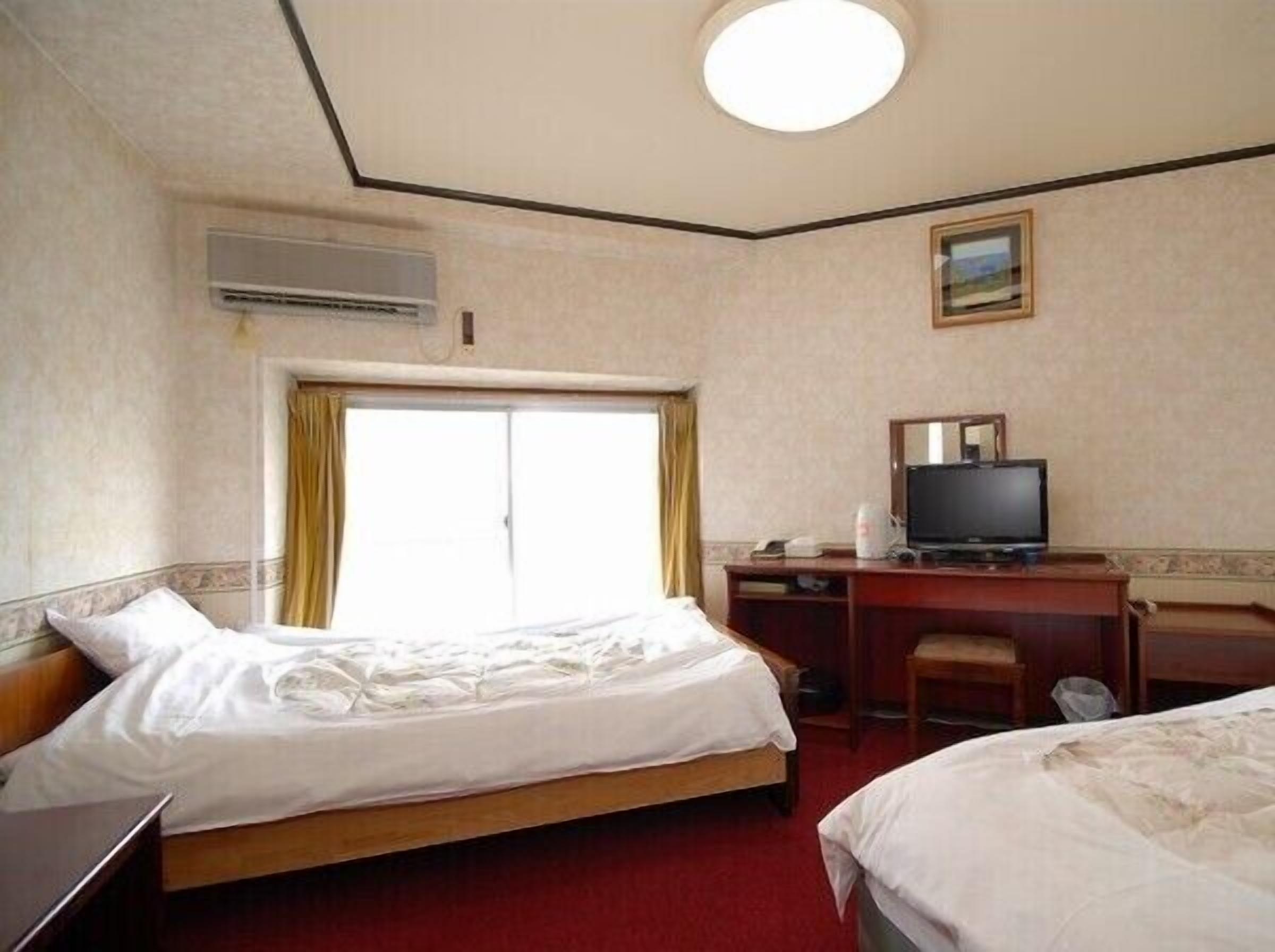 Ein Hotelzimmer mit zwei Betten, einem Schreibtisch mit Fernseher und einer Klimaanlage.