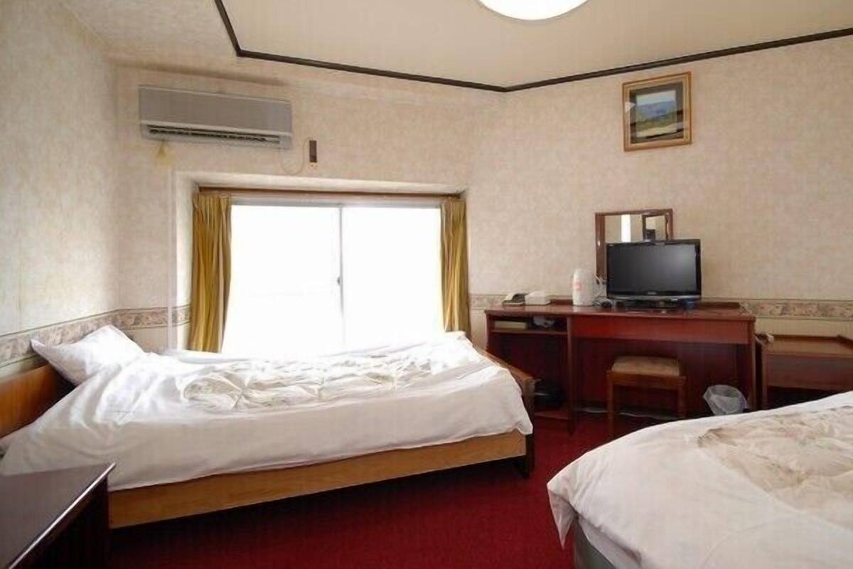 A hotel room with two beds, a desk with a television, and an air conditioning unit.