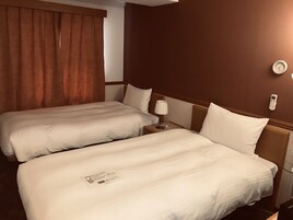 Una habitación de hotel con dos camas individuales, una mesita de noche con lámpara, un termostato y un teléfono en la pared.