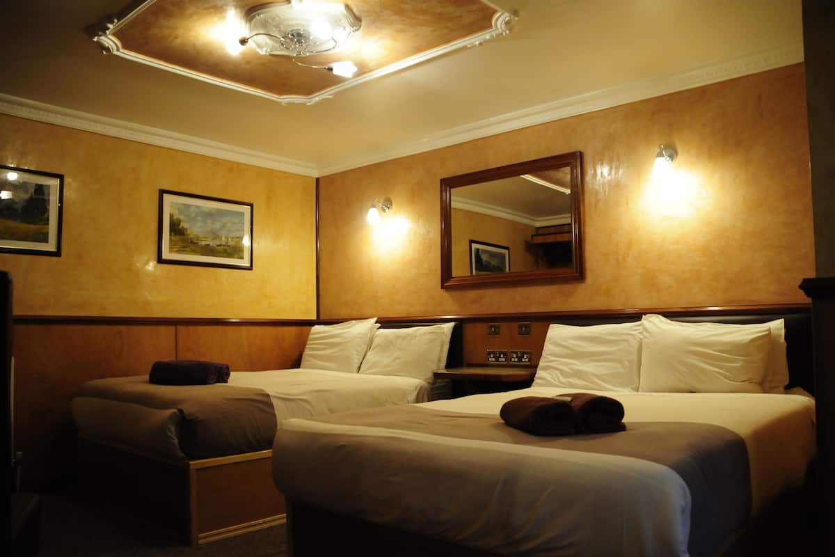 Une chambre d’hôtel avec deux lits, des têtes de lit en bois, un grand miroir et un luminaire au plafond.