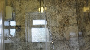 Une salle de bain avec un mur de douche en marbre, une douche fermée par des parois de verre et un lavabo blanc.