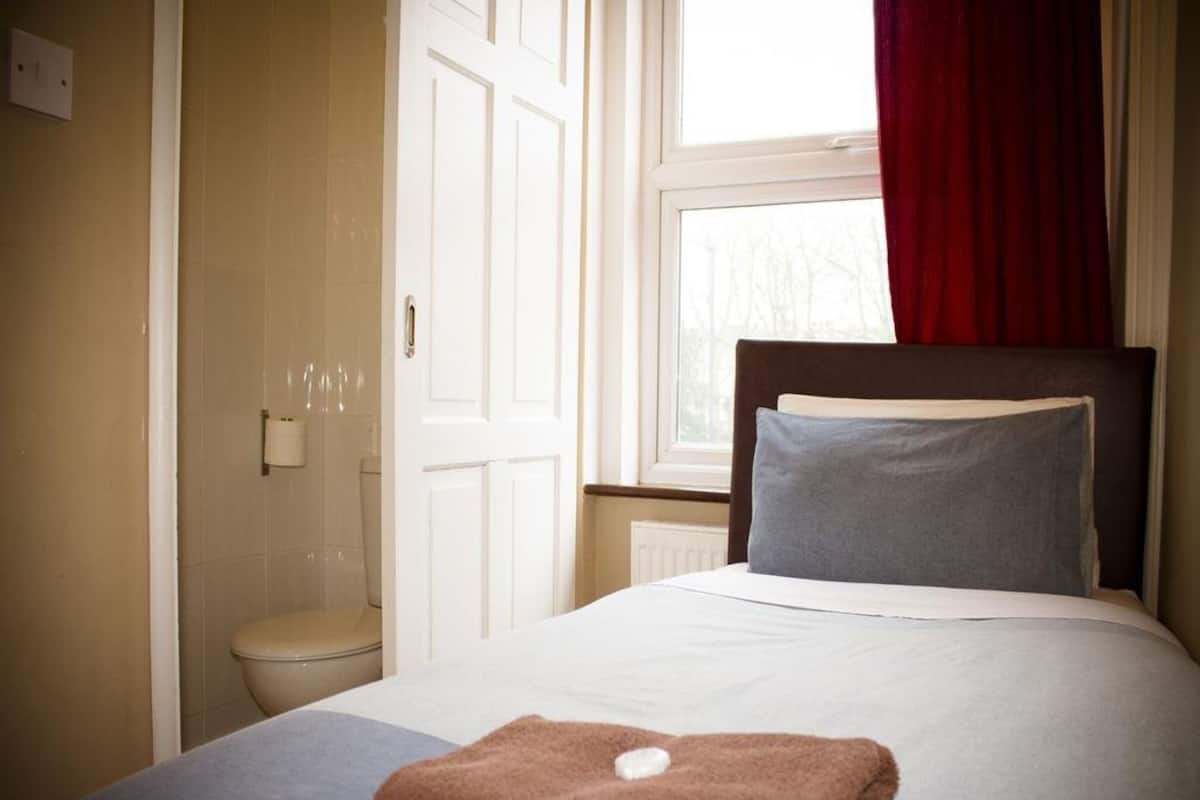 Une chambre à coucher avec un lit, une fenêtre ornée d’un rideau rouge et une porte blanche.