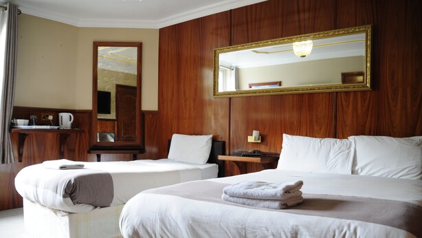 Une chambre d’hôtel avec deux lits, un mur recouvert de panneaux en bois, un grand miroir et une petite table avec une bouilloire.