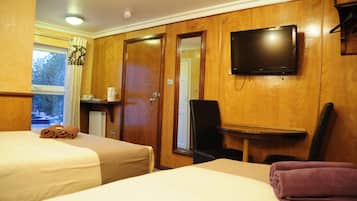 Habitación de hotel con dos camas, un televisor montado en la pared, un escritorio con una silla y una ventana con cortinas.