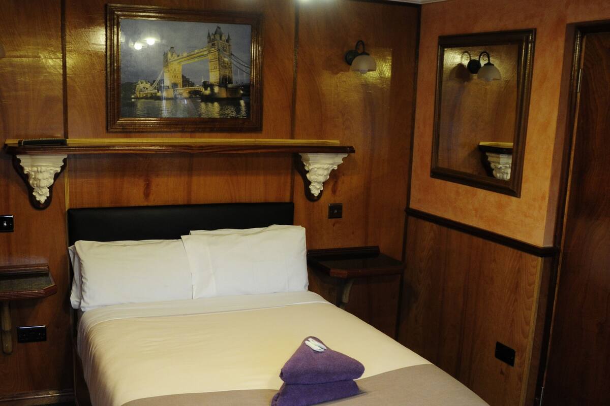 Une chambre d’hôtel avec un grand lit, une tête de lit en bois, un tableau représentant un pont et un lustre.
