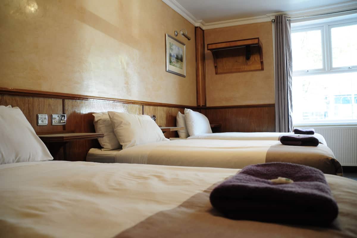 Une chambre d’hôtel avec deux lits, une tête de lit en bois, un tableau encadré au mur et une fenêtre avec des rideaux.