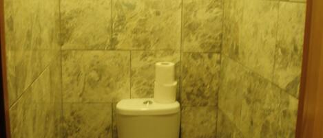 A bathroom with a toilet, marble tiles, and a roll of toilet paper on the floor.