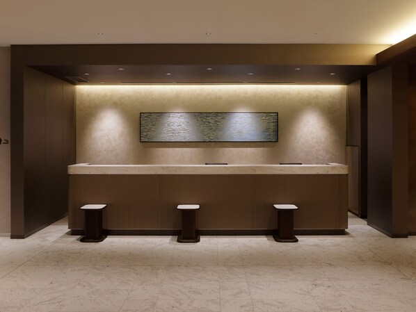 A modern restroom with a marble countertop, three stools, and a wall-mounted sink.