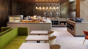 En moderne hotellobby med buffetområde, siddepladser og et dekorativt lysarmatur.