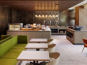 A modern hotel lobby with a buffet area, seating arrangements, and a decorative light fixture.