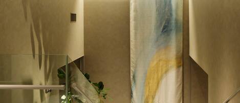Un interior moderno con una escalera de cristal, una pared color beige y un cuadro abstracto de gran tamaño.