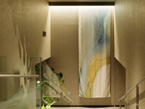 A modern interior with a glass staircase, a beige wall, and a large abstract painting. - Mitsui Garden Hotel Okayama (Okayama)
