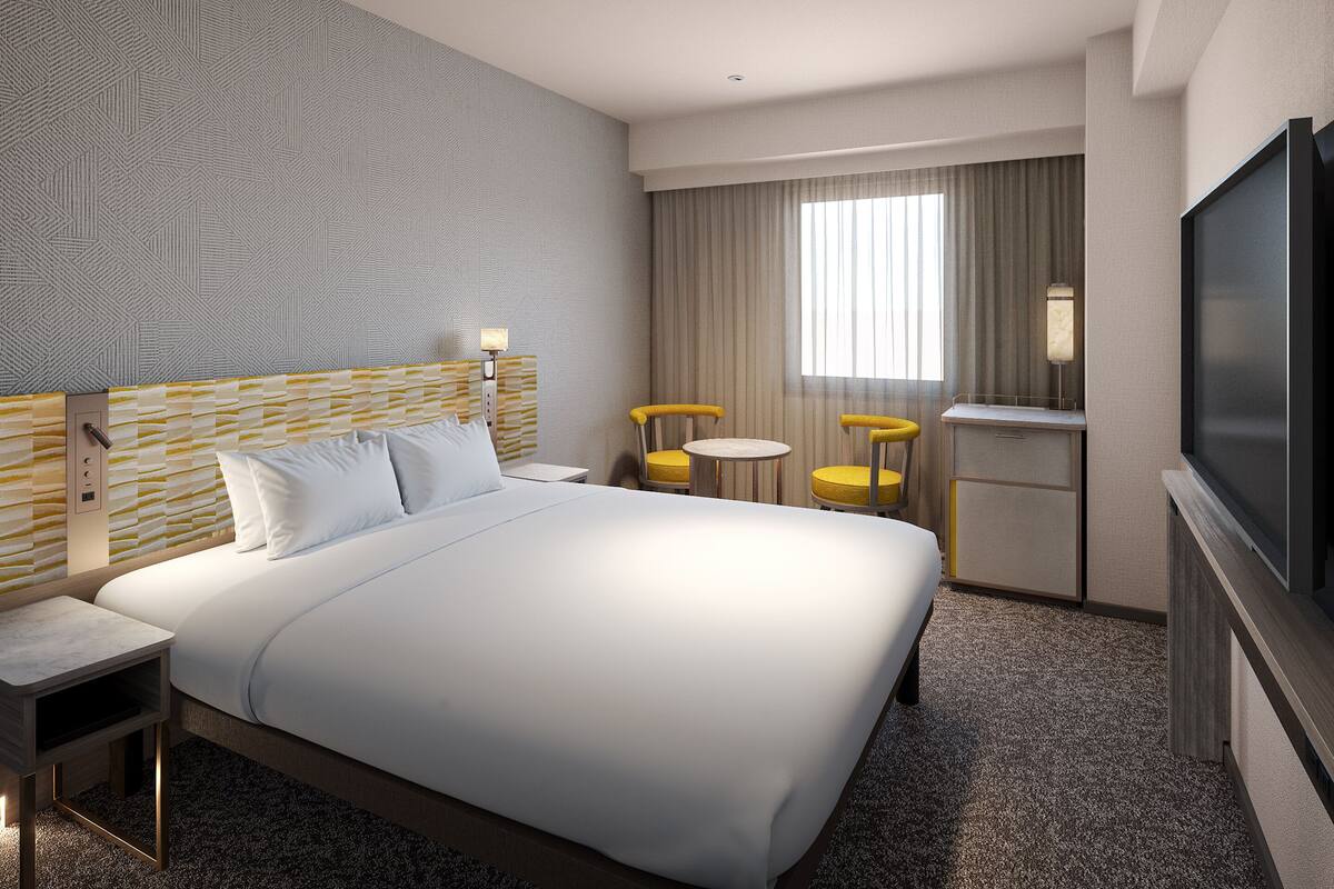 Una habitación de hotel con una cama grande, un escritorio, dos sillas, una mesita, un televisor y una ventana con cortinas.
