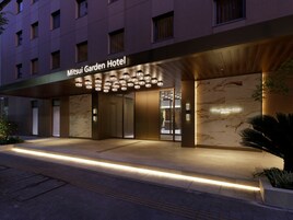 Exterior del Mitsui Garden Hotel, con fachada moderna, entrada iluminada y un detalle en pared de mármol.