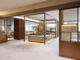 Un interior moderno con una zona de comedor central, un mostrador de recepción y un letrero que dice 'GARDEN CAFE'.