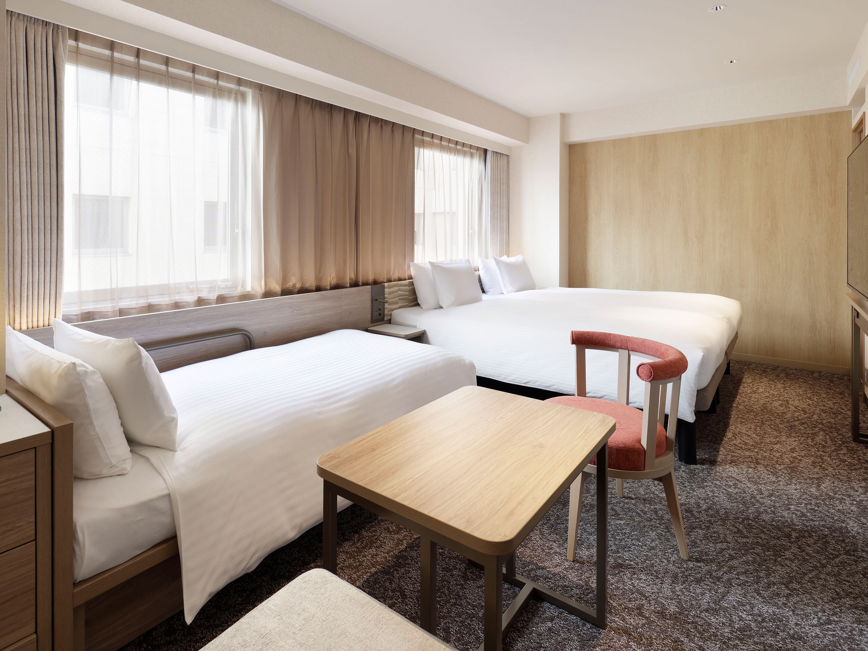 A hotel room with two beds, a desk, a chair, and a TV.