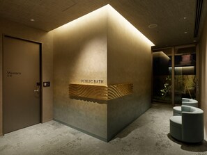 Casa de banho pública com indicação para mulheres, parede com textura e área de estar com divisória de vidro.