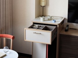 Habitación de hotel compacta con minibar, una mesita con un vaso y una silla.