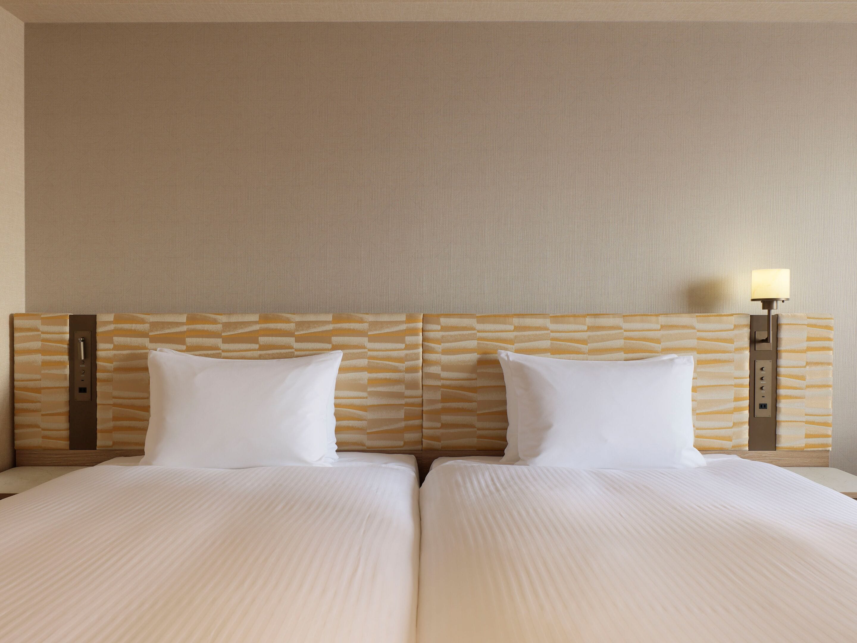 Habitación de hotel con cama doble, dos mesitas de noche y cabecero con textura.