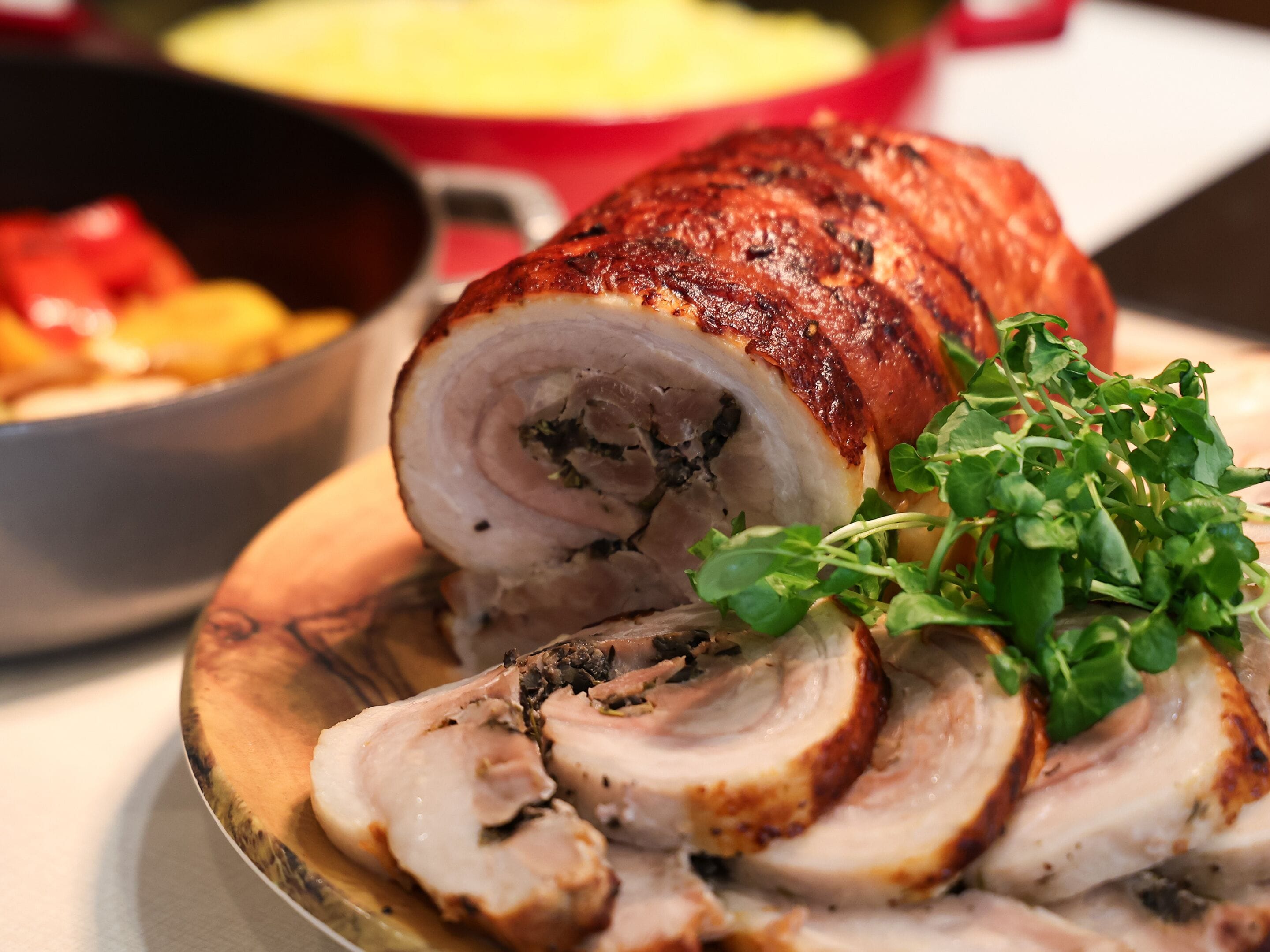 A roasted pork dish with a crispy exterior, sliced meat, and a garnish of greens on a plate.