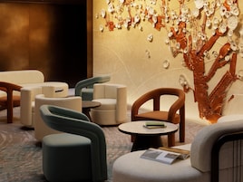 A modern lounge area with sofas and armchairs, a round table with a book, and a wall with abstract art.