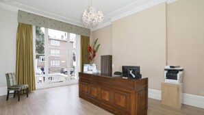 Un espace d’accueil avec un bureau en bois, une chaise, un lustre et une vue sur l’extérieur.