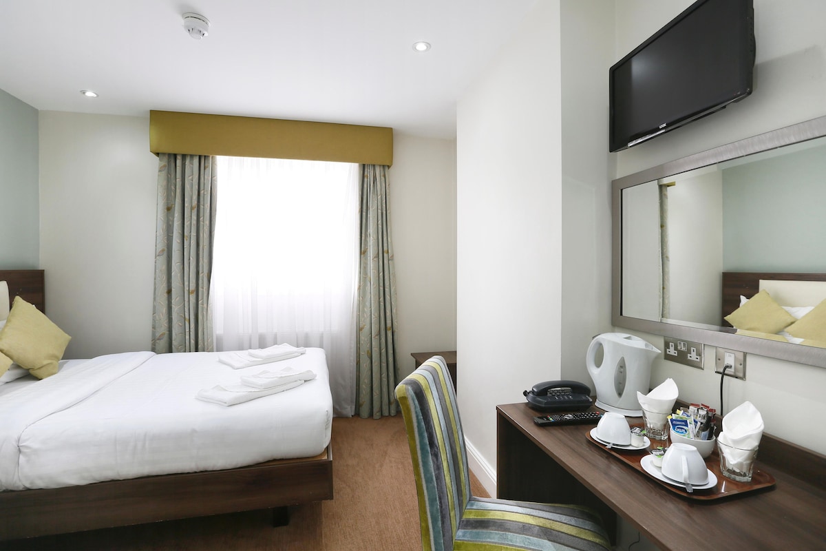 Habitación de hotel con cama, escritorio, teléfono, cafetera y espejo.