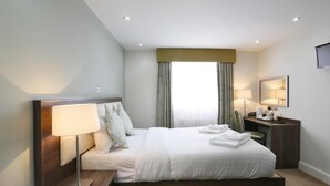 Une chambre d’hôtel moderne, dotée d’un grand lit, de lampes de chevet, d’un bureau avec une chaise et d’un téléviseur fixé au mur.