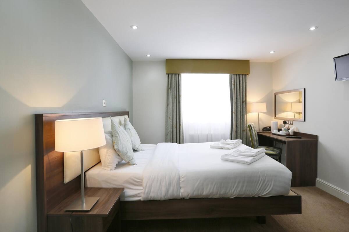 Habitación de hotel moderna con una cama grande, lámparas de noche, un escritorio con una silla y un televisor en la pared.