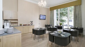 Un espace de restauration moderne avec des tables et des chaises rondes, un lustre et un téléviseur fixé au mur.