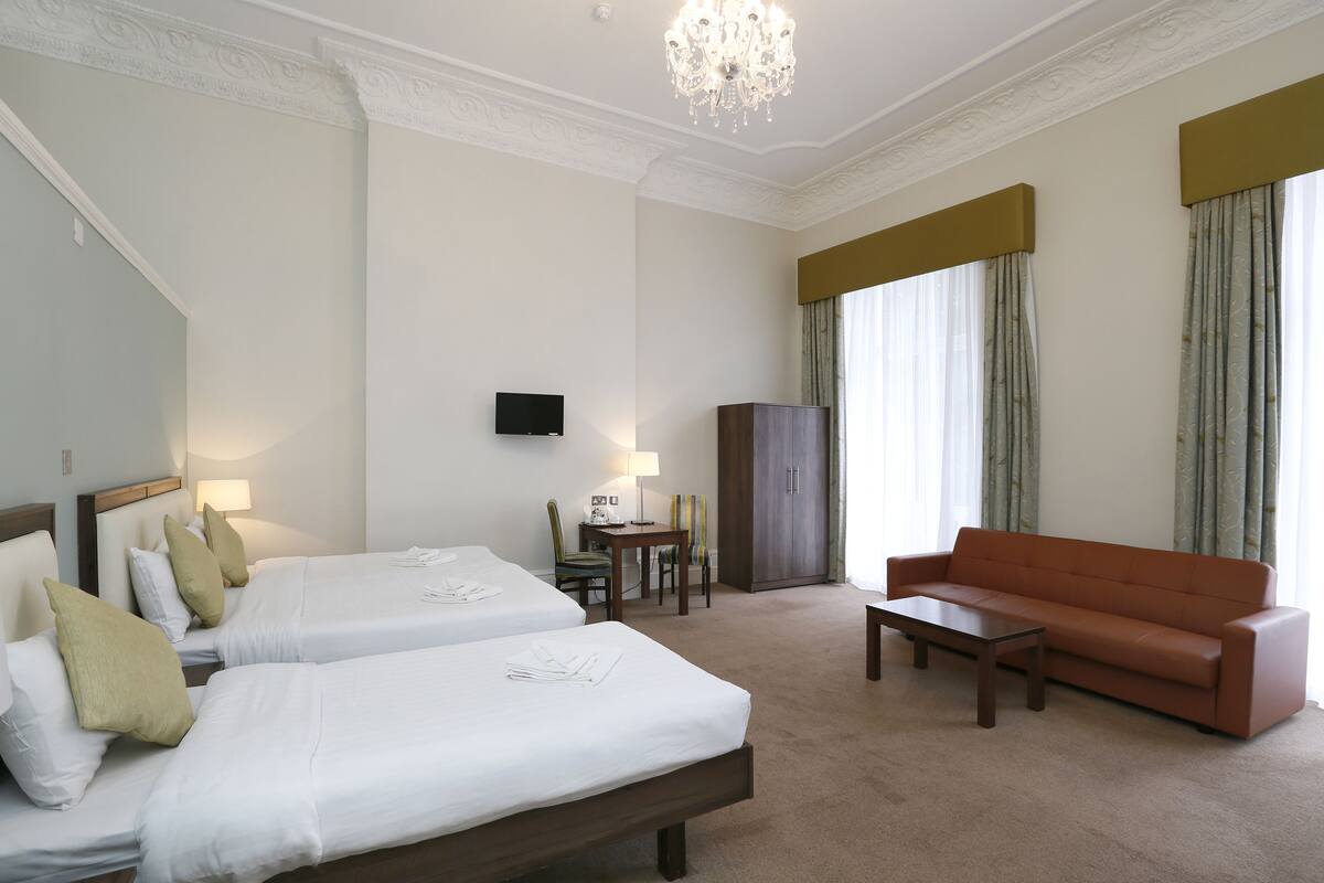 Habitación de hotel con dos camas, un sofá, un televisor, un escritorio y una araña.