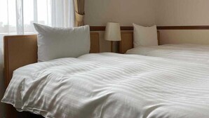 A hotel room with two beds, a nightstand, a lamp, and a window with curtains. - Toyoko Inn Asahikawa Ekimae Ichijo-dori (HOKKAIDO)