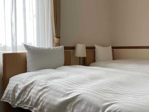 A hotel room with two beds, a nightstand, a lamp, and a window with curtains. - Toyoko Inn Asahikawa Ekimae Ichijo-dori (HOKKAIDO)