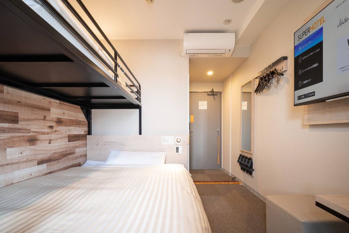Habitación con literas, cabecero de madera, mesita de noche pequeña y aire acondicionado de pared.