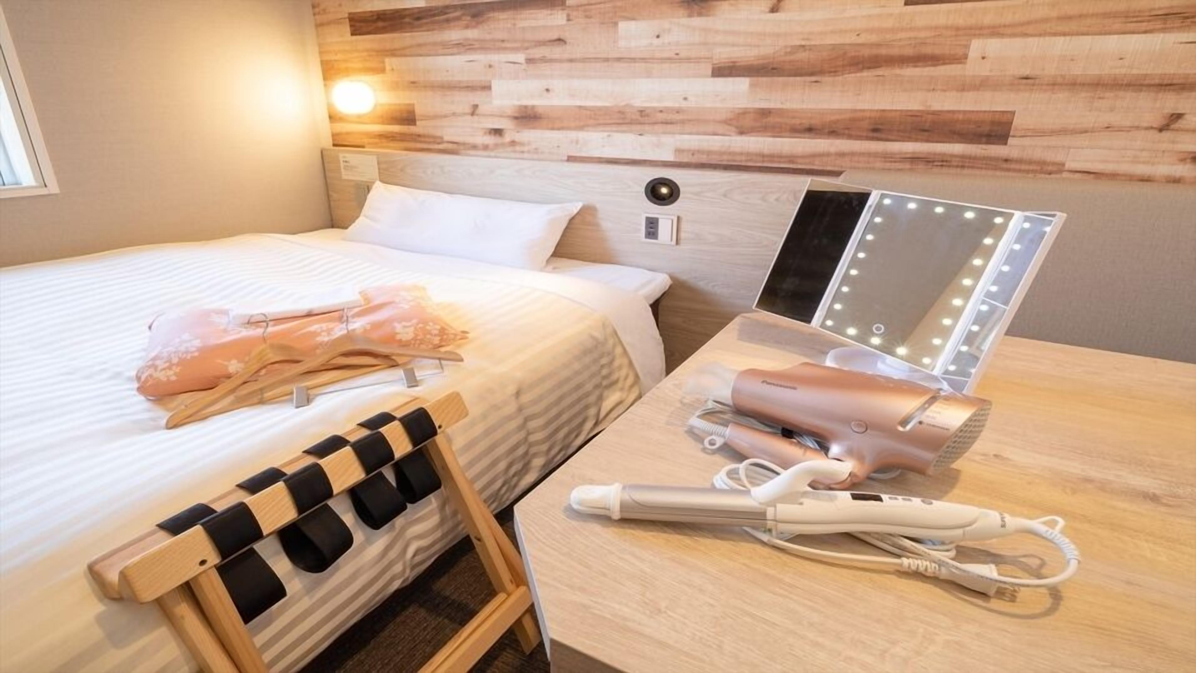 Ein Hotelzimmer mit einem Bett, einem Schminktisch mit Spiegel und Beleuchtung sowie einem Fön auf dem Tisch.