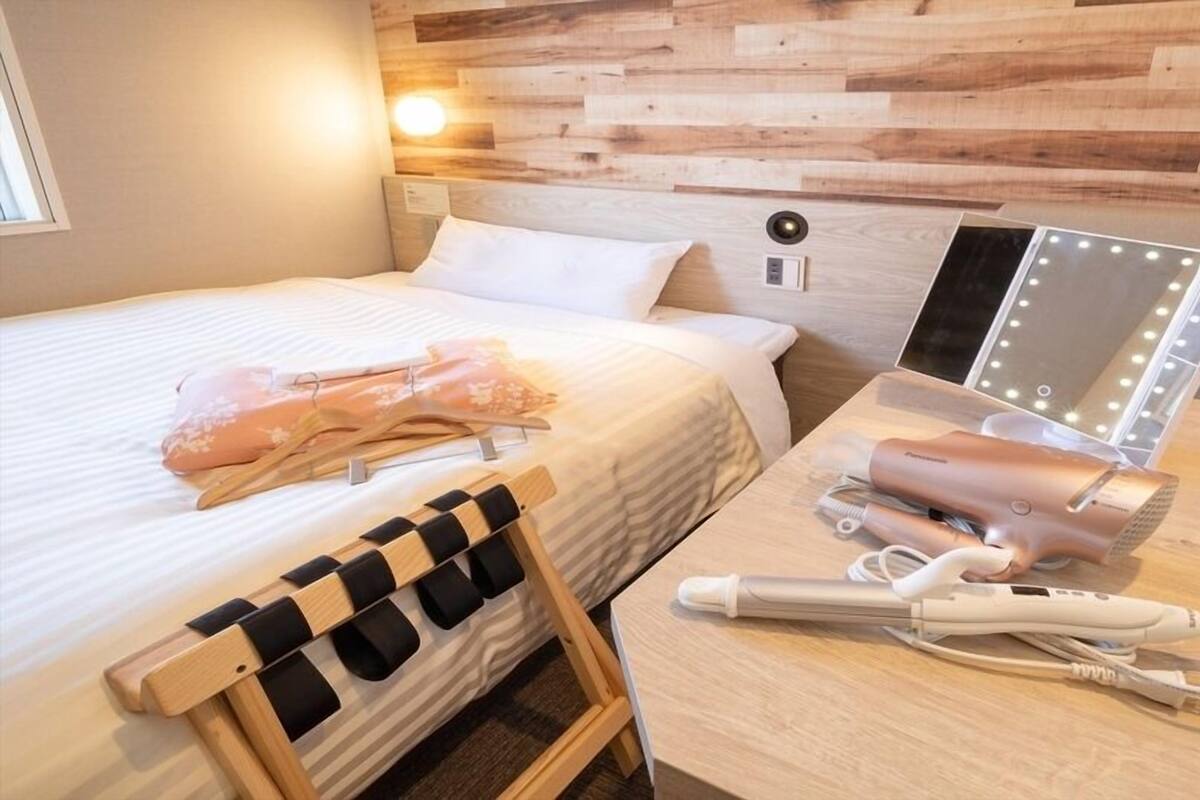 Una habitación de hotel con una cama, un tocador con espejo e iluminación, y un secador de pelo sobre la mesa.