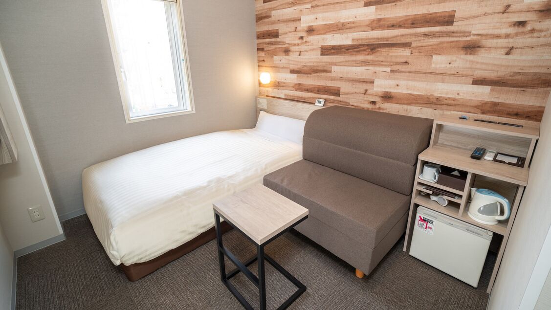Ein kleines Zimmer mit einem Bett, einem kleinen Tisch, einer Sitzecke, einer Mikrowelle und einem kleinen Kühlschrank.