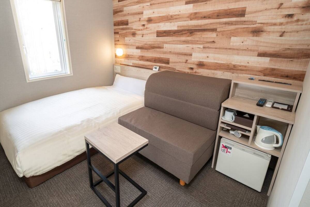 Una habitación pequeña con cama, una mesita, un sofá, microondas y refrigerador compacto.