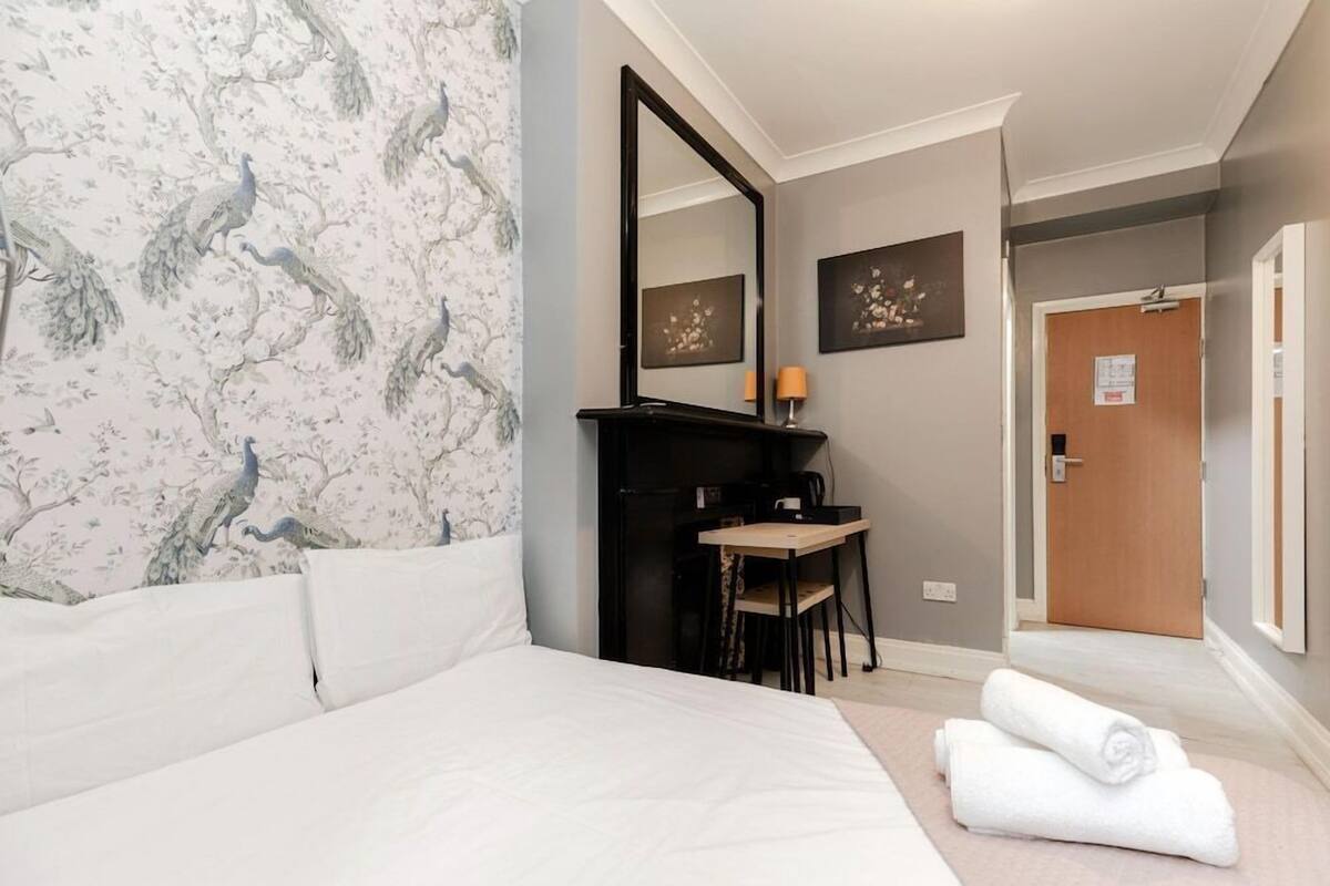 Une chambre d’hôtel avec un lit, un bureau et une chaise, un miroir et deux tableaux encadrés au mur.